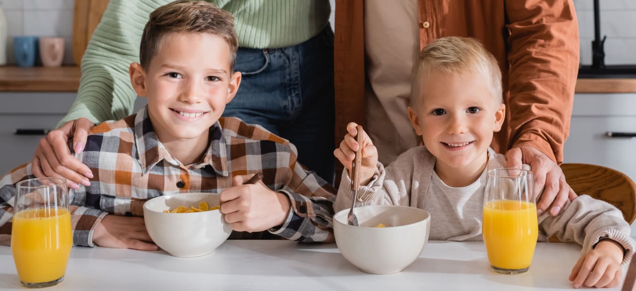 Two young boys sitting at the table eating breakfast.