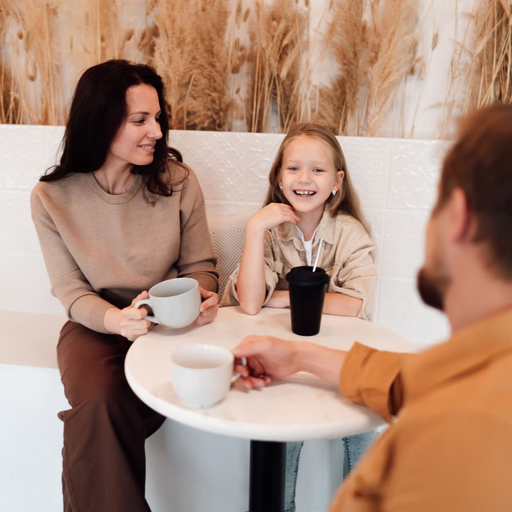 A family of three sits at a coffee shop enjoying beverages.