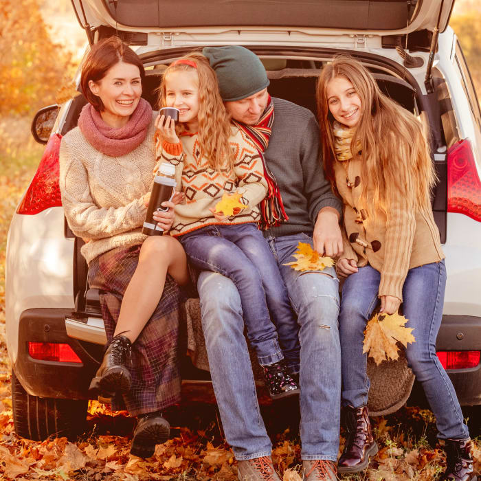 A family sits outside in the trunk of a car in the autumn.